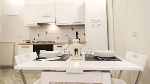Une cuisine moderne avec des meubles blancs, une table à manger dressée avec des assiettes, des verres et une lanterne allumée.