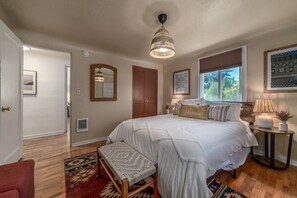 A bedroom with a large bed, a wooden bench, a standing lamp, and a window with blinds. - Cozy Boho Bungalow in Eugene! (Eugene)
