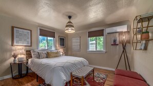 Um quarto com uma cama grande, um banquinho, um sofá vermelho e um tapete estampado.