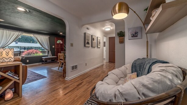 Uma sala de estar moderna com piso de madeira, área de estar acolchoada e uma mesa de jantar com cadeiras.