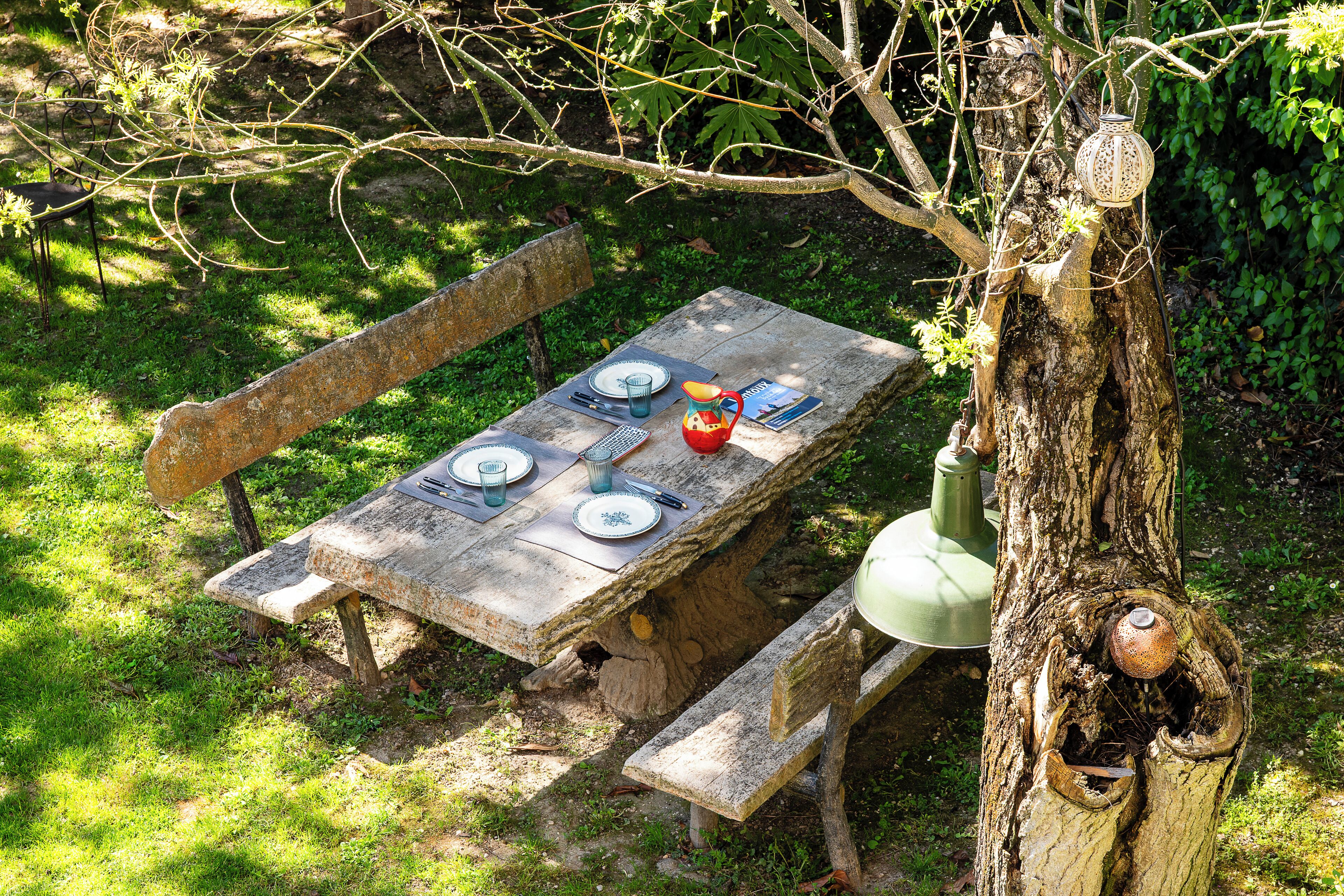 Mesa de piquenique montada ao ar livre, com banco, rodeada por vegetação.