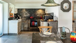 A rustic kitchen with exposed wooden beams, a chalkboard wall, and a dining area with a marble table.