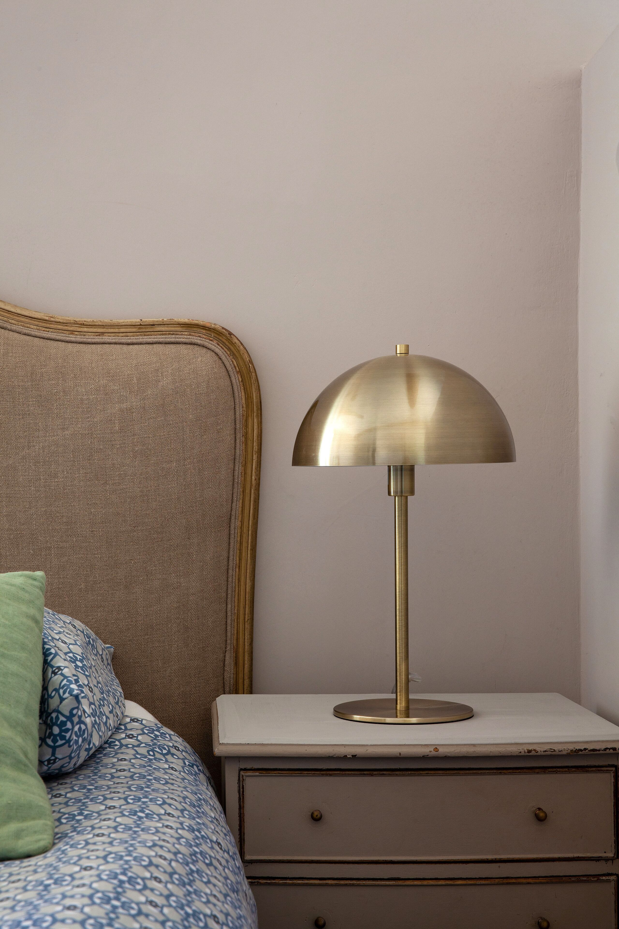 A bedside table with a lamp, a bed with patterned bedding, and a green pillow.