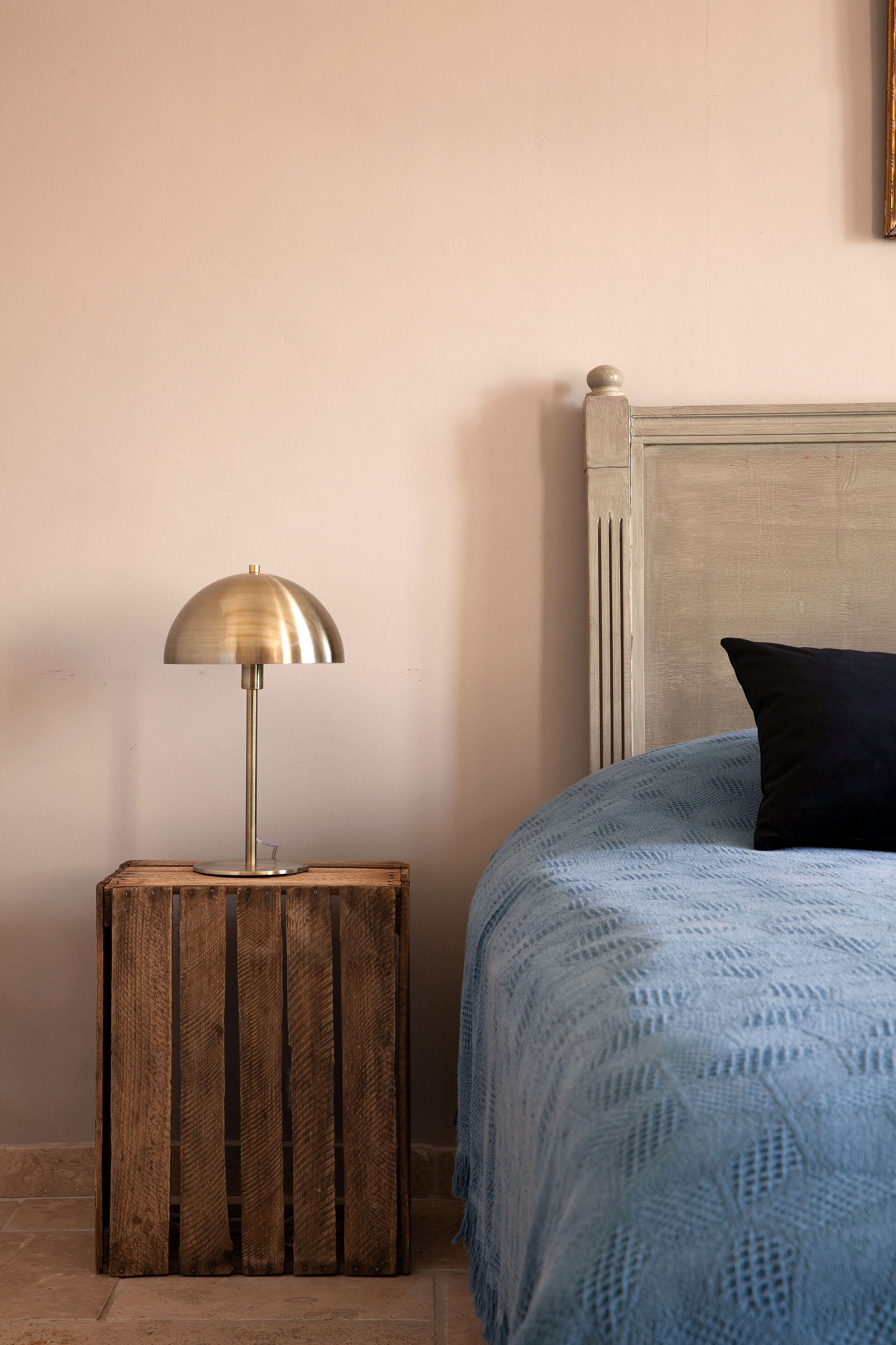 A bedroom with a wooden nightstand, a lamp, a bed with a blue blanket, and a headboard.
