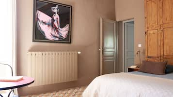 Ein Schlafzimmer mit einem Bett, einem Heizkörper, einem Holzschrank, einem Tisch mit Stuhl und einem gerahmten Kunstwerk an der Wand.
