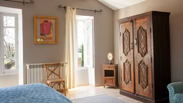Un dormitorio con cama, armario de madera, radiador, silla y ventana con cortinas.