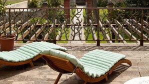 A terrace with two wooden lounge chairs and a table, overlooking a vineyard and a scenic landscape.