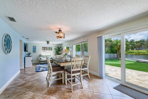 A spacious dining area with a wooden table and chairs, a ceiling fan, and a view of a green lawn through large sliding glass doors. - Riverfront Home w/ Putting Green & Boat Dock! (New Port Richey)