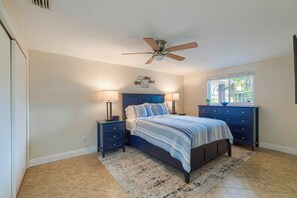 A bedroom with a bed, two bedside tables, a ceiling fan, a window, and a nightstand with a lamp.