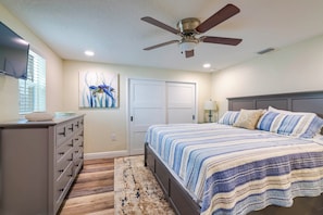 A bedroom with a bed, a dresser, a ceiling fan, a painting, and a door. - Riverfront Home w/ Putting Green & Boat Dock! (New Port Richey)