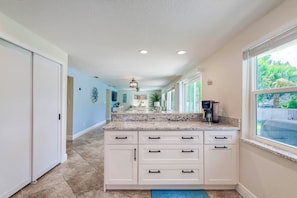 A kitchen with a central island, white cabinetry, and a view of greenery outside. - Riverfront Home w/ Putting Green & Boat Dock! (New Port Richey)