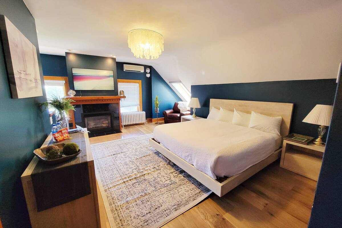 A bedroom with a large bed, a fireplace, a chandelier, and a view of the outdoors.