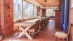 A spacious dining area with a large wooden table and chairs, brick walls, and large windows offering a view of trees. - Historic GG Barnum Mansion by Heirloom Boutique Collection (Duluth)