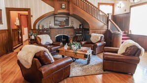 A spacious living room with leather sofas, a wooden coffee table, and a grand staircase. - Historic GG Barnum Mansion by Heirloom Boutique Collection (Duluth)