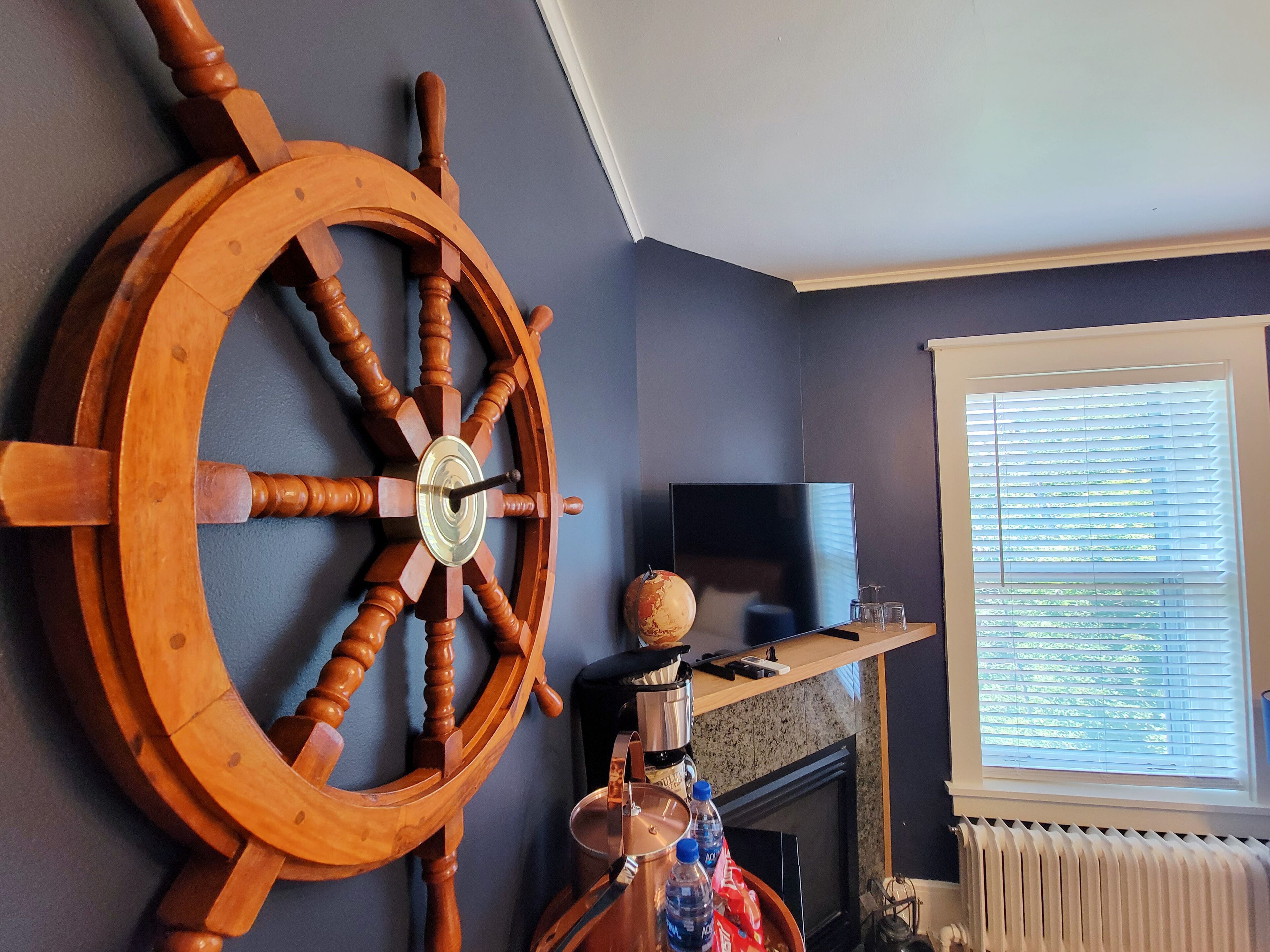 Una habitación con una gran rueda de barco de madera, un televisor de pantalla plana, chimenea y una ventana con persianas.