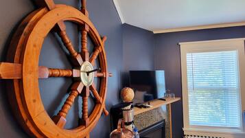 Una habitación con una gran rueda de barco de madera, un televisor de pantalla plana, chimenea y una ventana con persianas.
