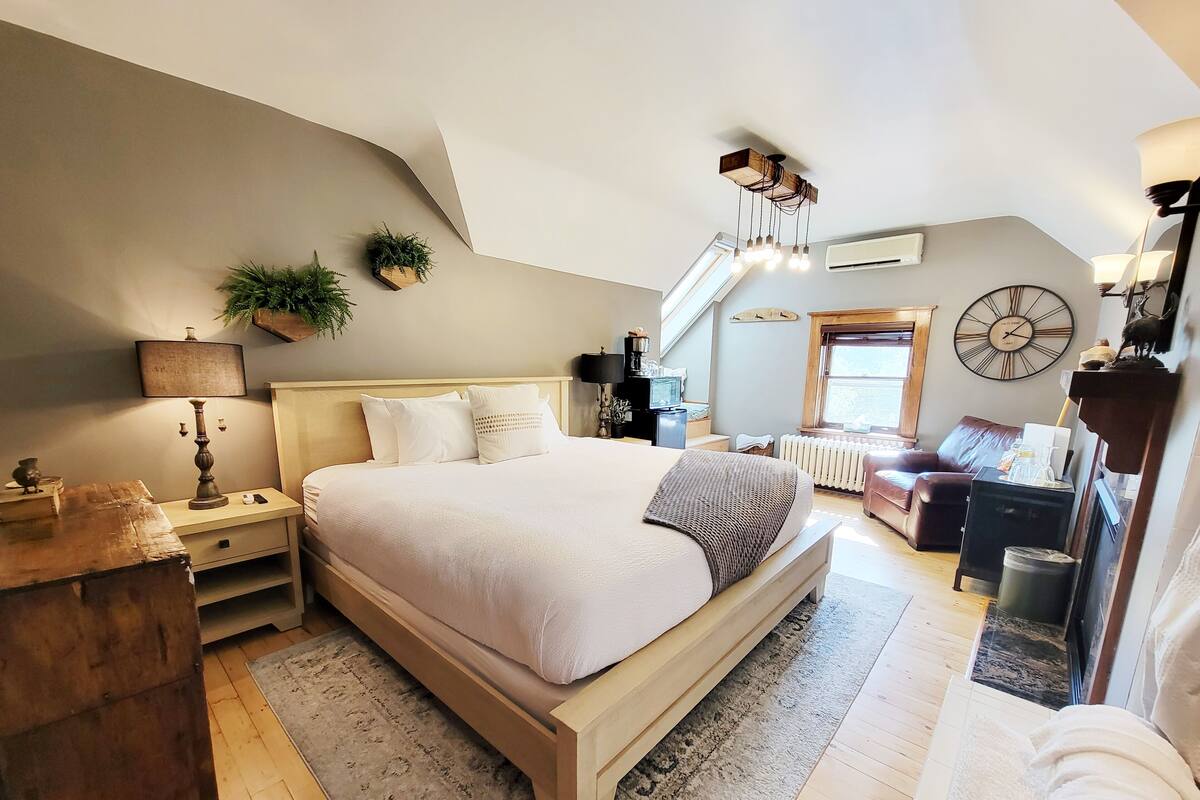 A bedroom with a large bed, a wooden nightstand, a desk, a chair, and a window.