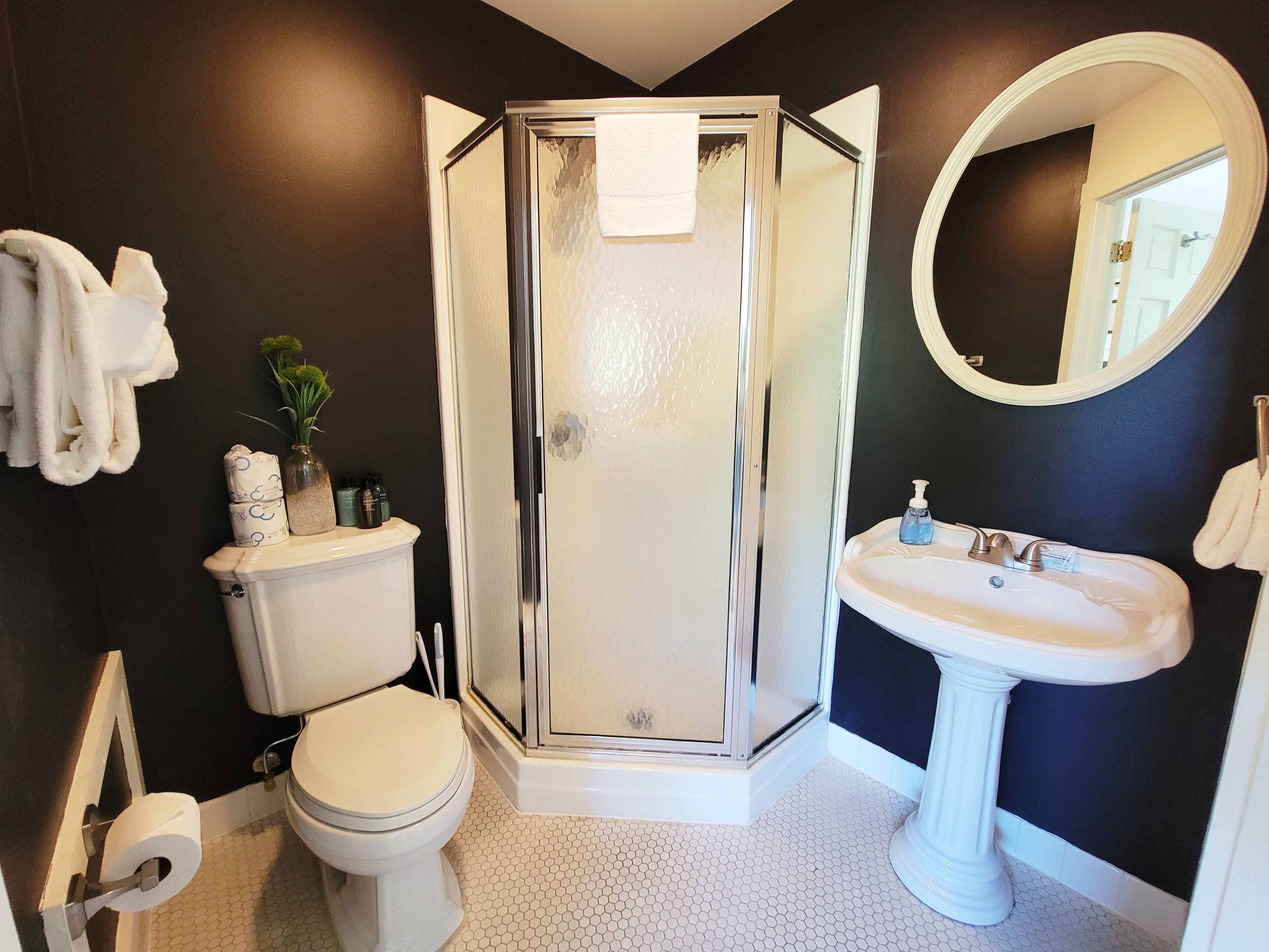 A bathroom with a toilet, a shower enclosure, a sink, and a mirror.