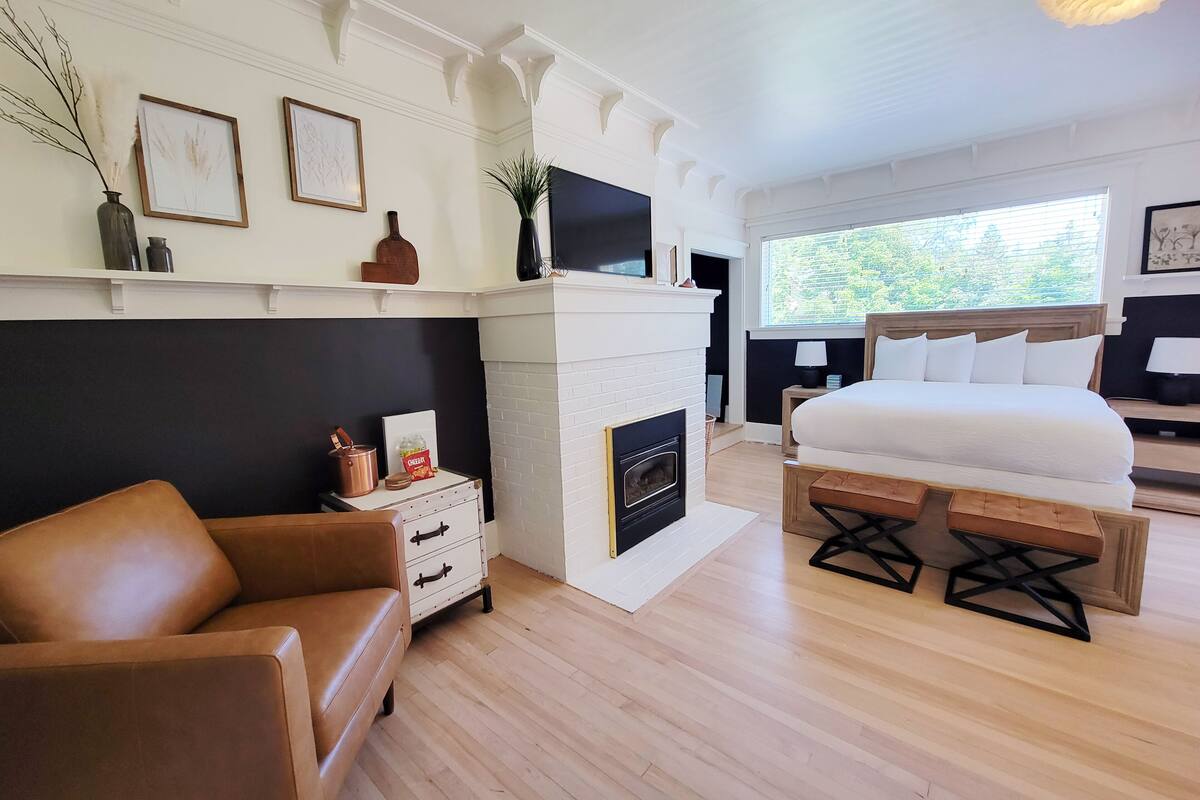 A modern bedroom with a white fireplace, a large bed, a sofa, and a nightstand.