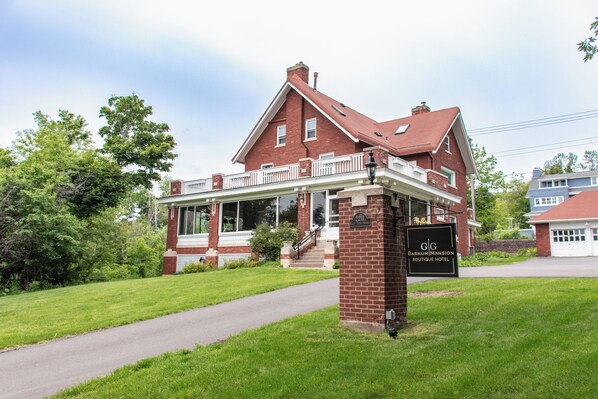 A large brick building with a porch, a sign for Barnum Mansion Boutique Hotel, and a well-maintained lawn.