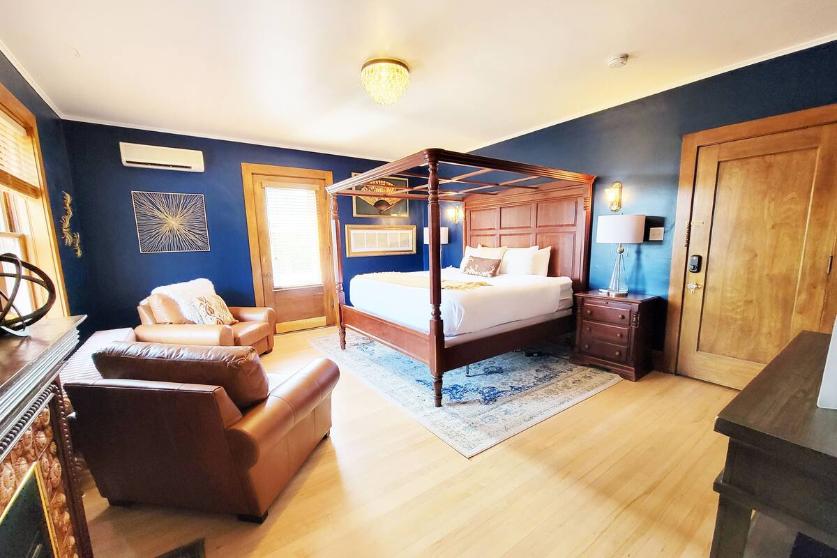 A bedroom with a four-poster bed, a wooden nightstand, a leather armchair, and a blue rug.
