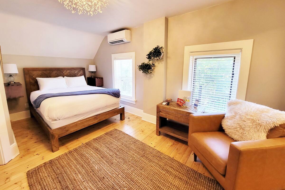 A bedroom with a wooden bed, a nightstand, a chair, a window with blinds, and a ceiling light fixture.