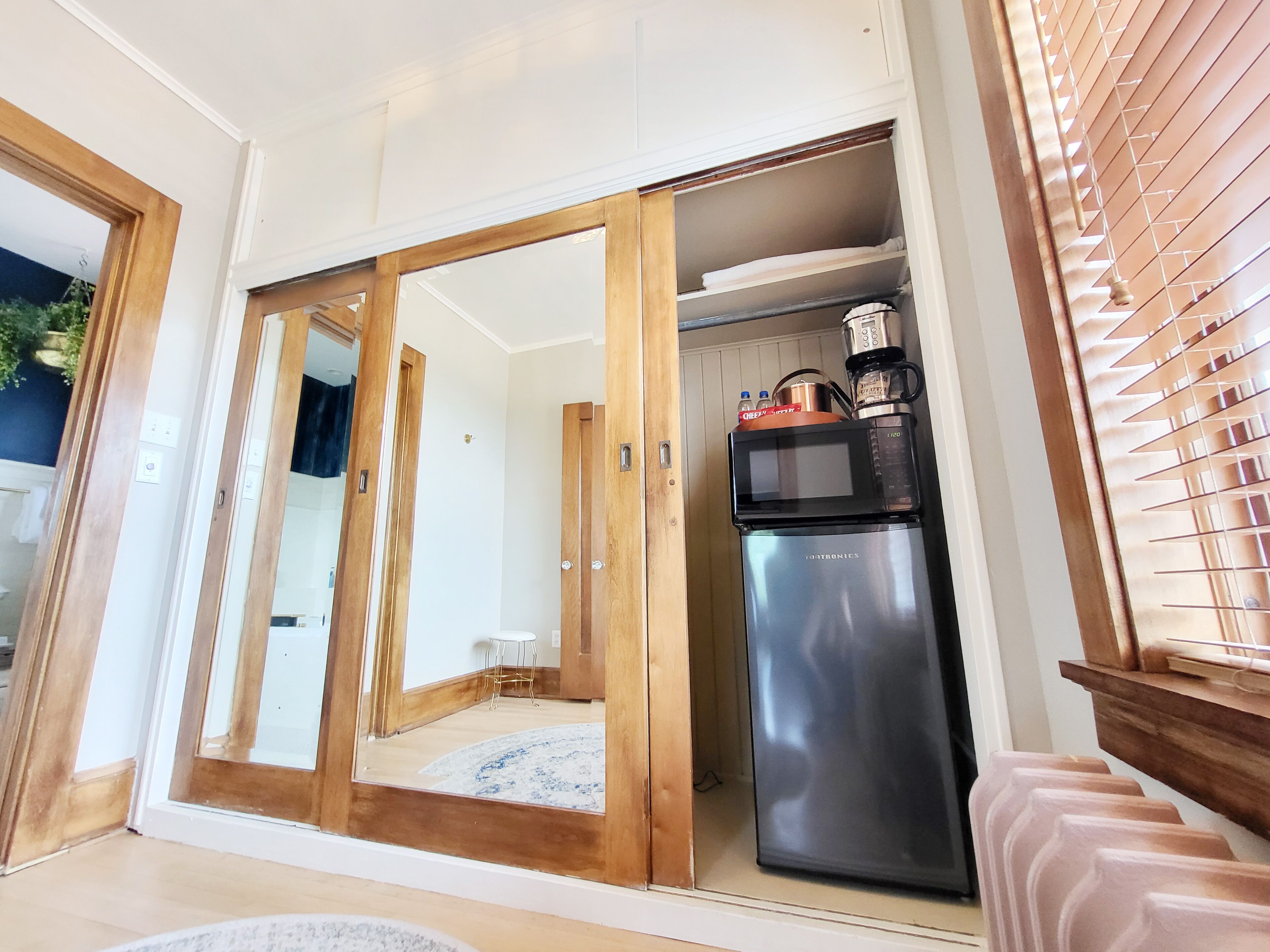 A compact kitchen with a built-in microwave, stainless steel refrigerator, and a coffee maker on top.