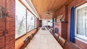 A long wooden dining table with chairs, a brick fireplace, and large windows along the walls. - Historic GG Barnum Mansion by Heirloom Boutique Collection (Duluth)
