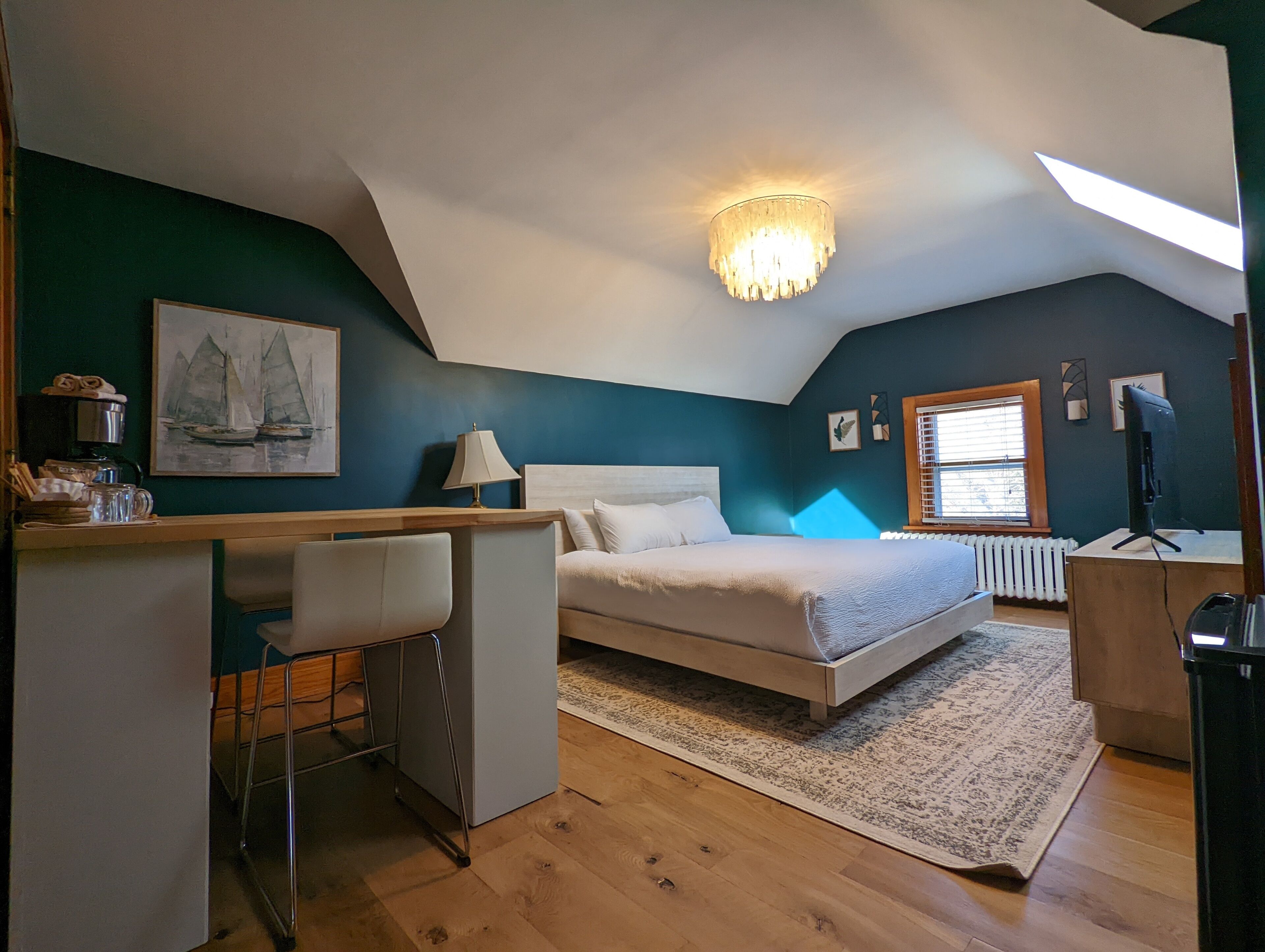 A bedroom with a bed, desk, chair, and a painting on the wall.