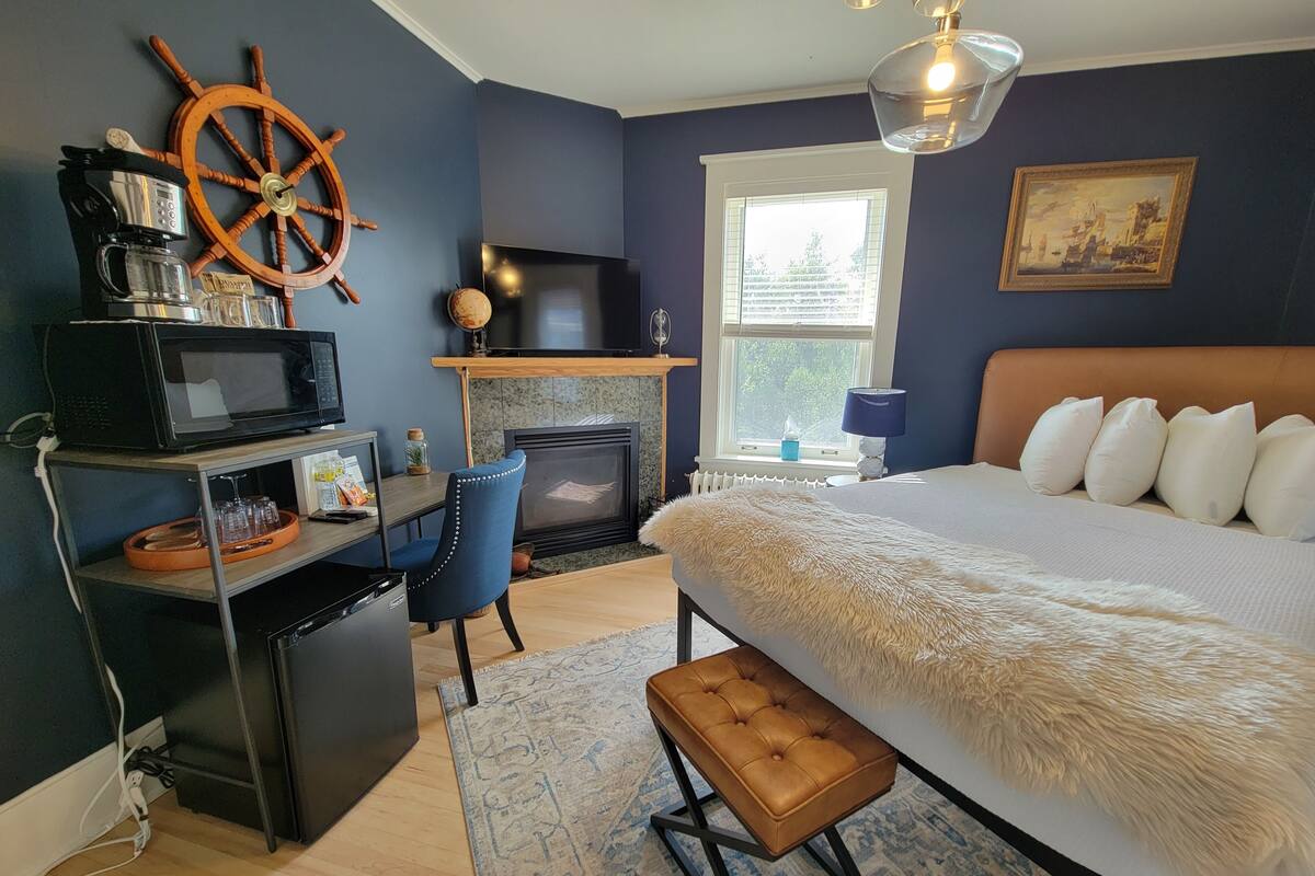 A bedroom with a bed, a desk, a television, a fireplace, and a window.