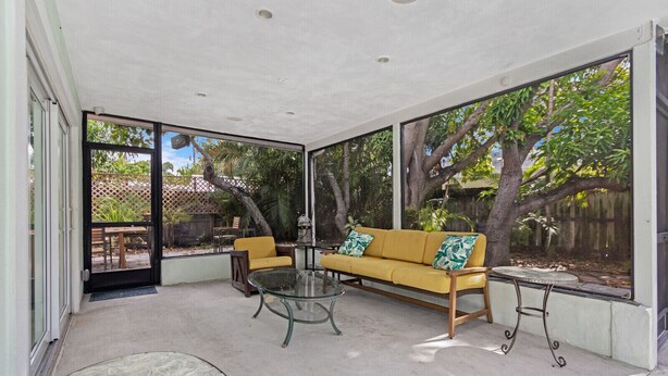A covered patio area with a yellow sofa, a glass table, and a small round table. - Heated Pool I Soundproof Home I Firepit I 630Mbps (Hollywood)