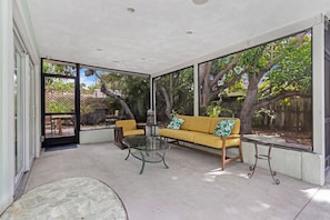 Ein überdachter Patio-Bereich mit einem gelben Sofa, einem Glastisch und einem kleinen runden Tisch.