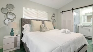 A bedroom with a bed, bedside table, lamp, and a view of the bathroom. - Heated Pool I Soundproof Home I Firepit I 630Mbps (Hollywood)