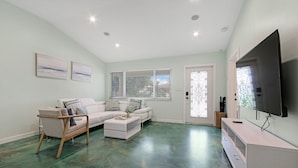 A living room with a white sofa, a wooden chair, a coffee table, and a TV on a stand. - Heated Pool I Soundproof Home I Firepit I 630Mbps (Hollywood)