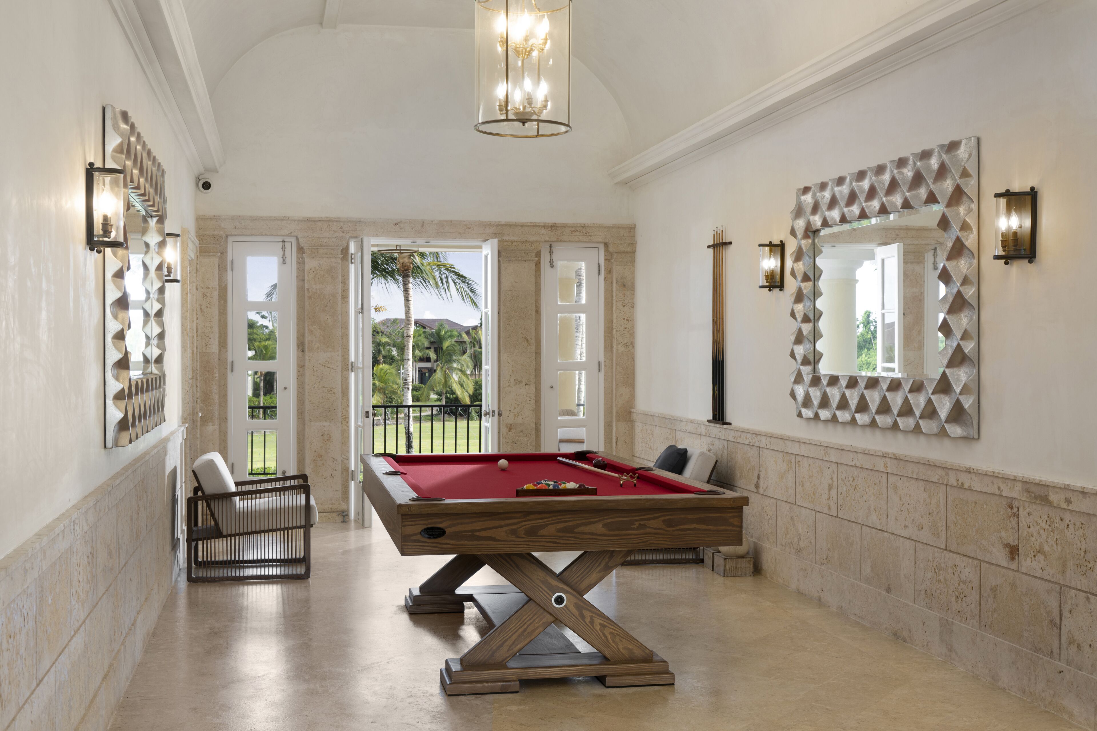 A pool table in a spacious room with a view of a garden and palm trees.