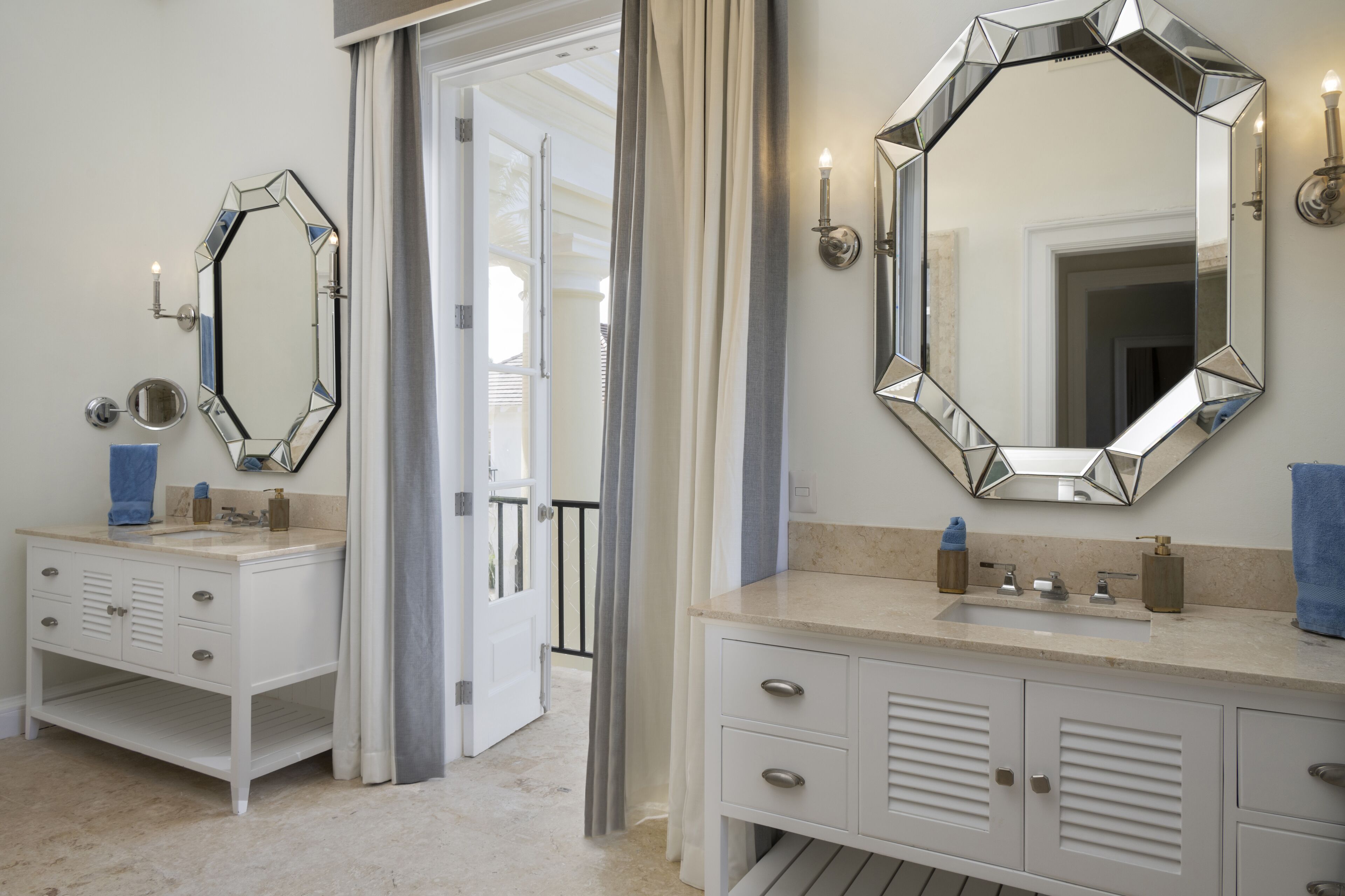 A bathroom with two sinks, each with a mirror, a towel, and a soap dispenser. There is a door leading to another room.