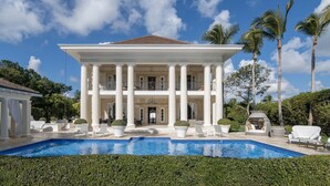 A large, white colonial-style building with a swimming pool in front.