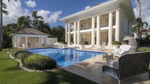 A large house with a swimming pool, outdoor seating, and palm trees.