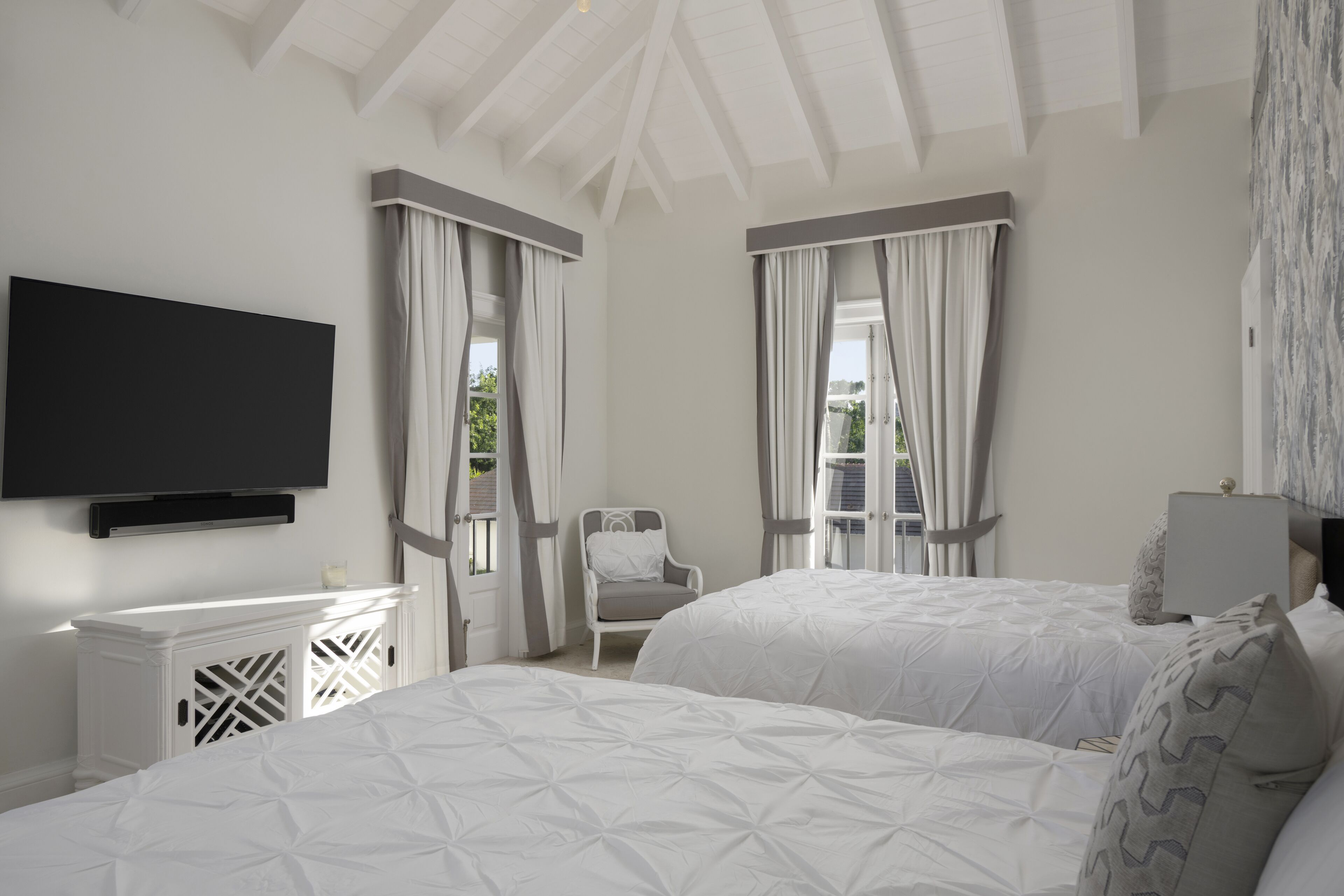 A bedroom with two beds, a TV, a chair, and a window with curtains.