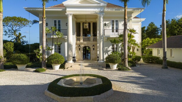 A large, two-story building with a symmetrical facade, a central entrance with a fountain, and a balcony on the upper floor.