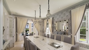 A dining area with a long table, chairs, chandeliers, and a large mirror.