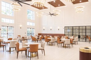 A spacious indoor area with multiple seating arrangements, including round tables and chairs, and a ceiling fan. - MONTREAL SUITES ORLANDO by IHG (Orlando)