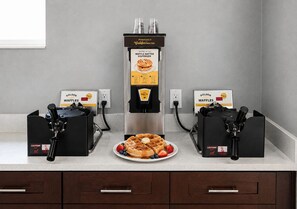 Una encimera de cocina con dos máquinas para hacer gofres y un dispensador de masa para gofres.