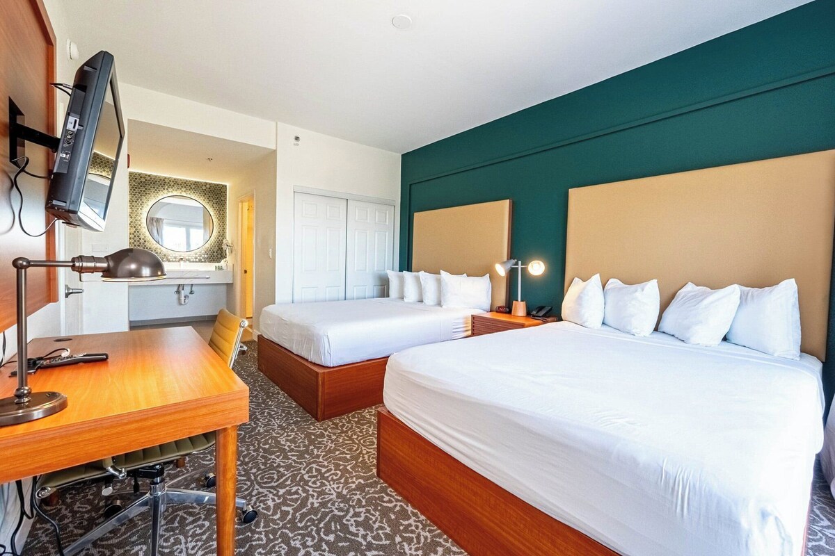 A hotel room with two beds, a desk, a TV, and a mirror.