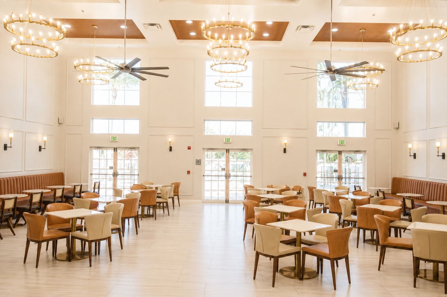 Un vaste espace dédié à la salle à manger, doté de nombreuses tables et chaises, de ventilateurs de plafond et baigné de lumière naturelle grâce à de grandes fenêtres.