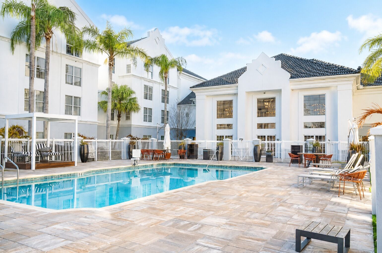 A swimming pool with lounge chairs and umbrellas, surrounded by white buildings with large windows.