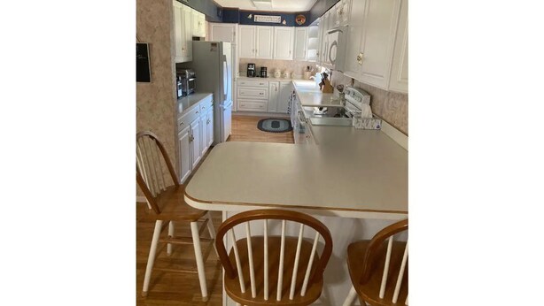 A kitchen with white cabinets, a central island, and wooden chairs. - Cozy 3-bedroom 2 bathroom house (Russell)