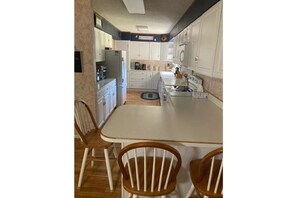 Una cocina con armarios blancos, una isla central y sillas de madera.