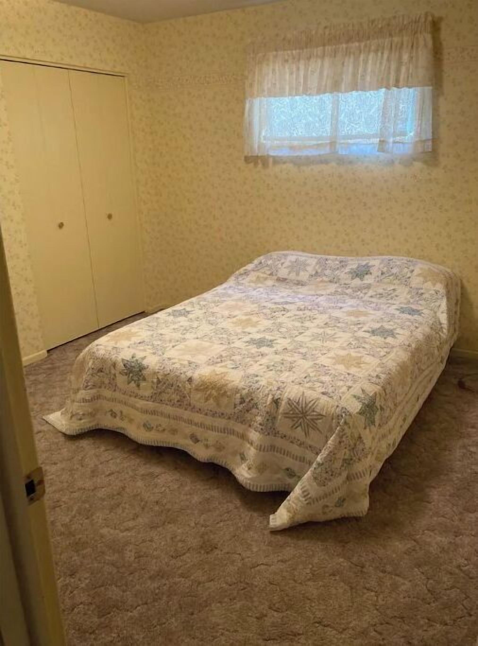 A bedroom with a bed, carpeted floor, a door, and a window with a curtain.