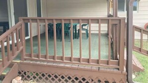 A covered patio area with a wooden railing, a table with chairs, and a door leading to the interior. - Cozy 3-bedroom 2 bathroom house (Russell)
